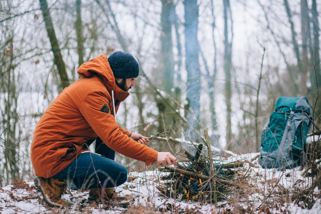 Mężczyzna rozpalający ognisko w trakcie zimowej wyprawy survivalowej